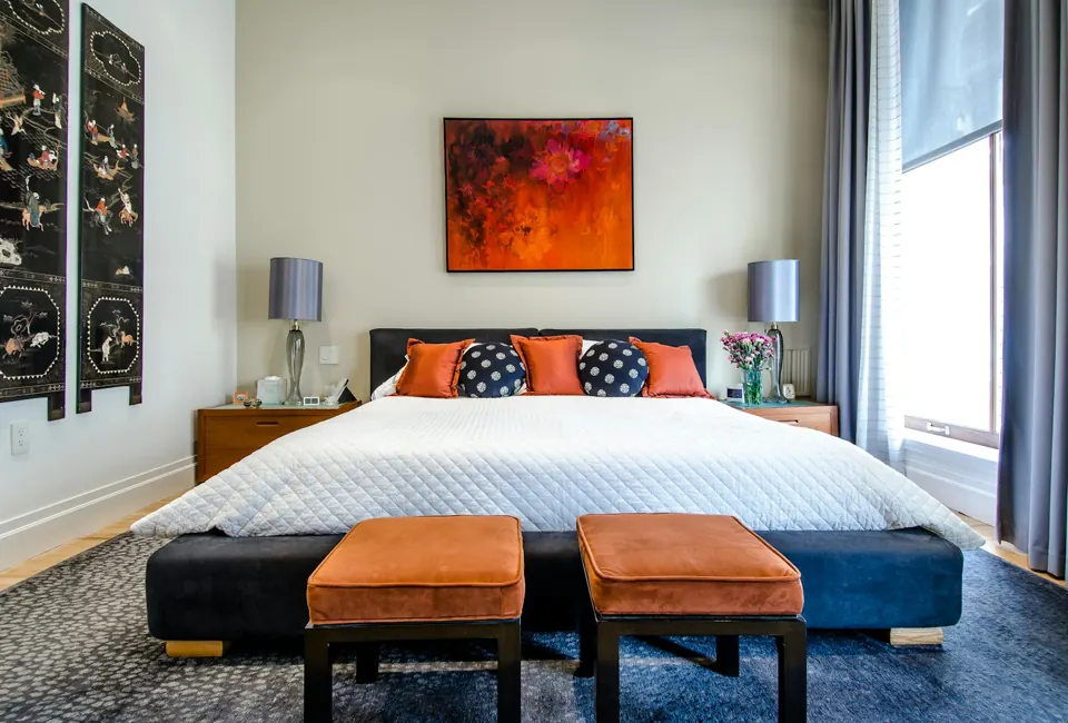 Bedroom with a blue upholstered bed, orange stools and colourful artwork