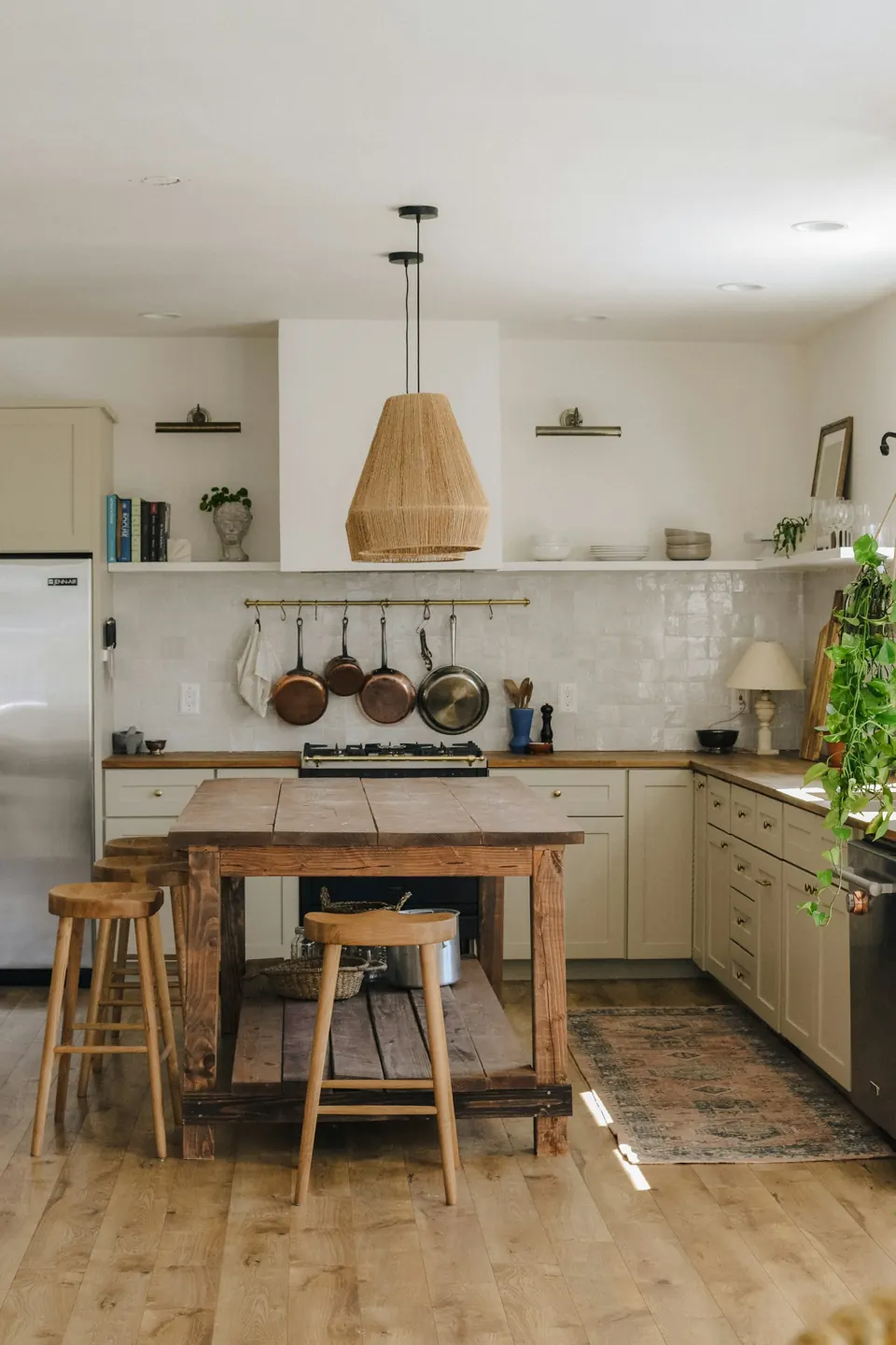 Cream kitchen with a woven pendant, timber island and hanging pans